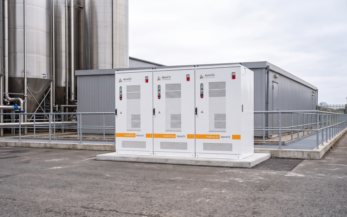 Drie batterijkasten op een bedrijfsterrein naast de silo's van een procesbedrijf