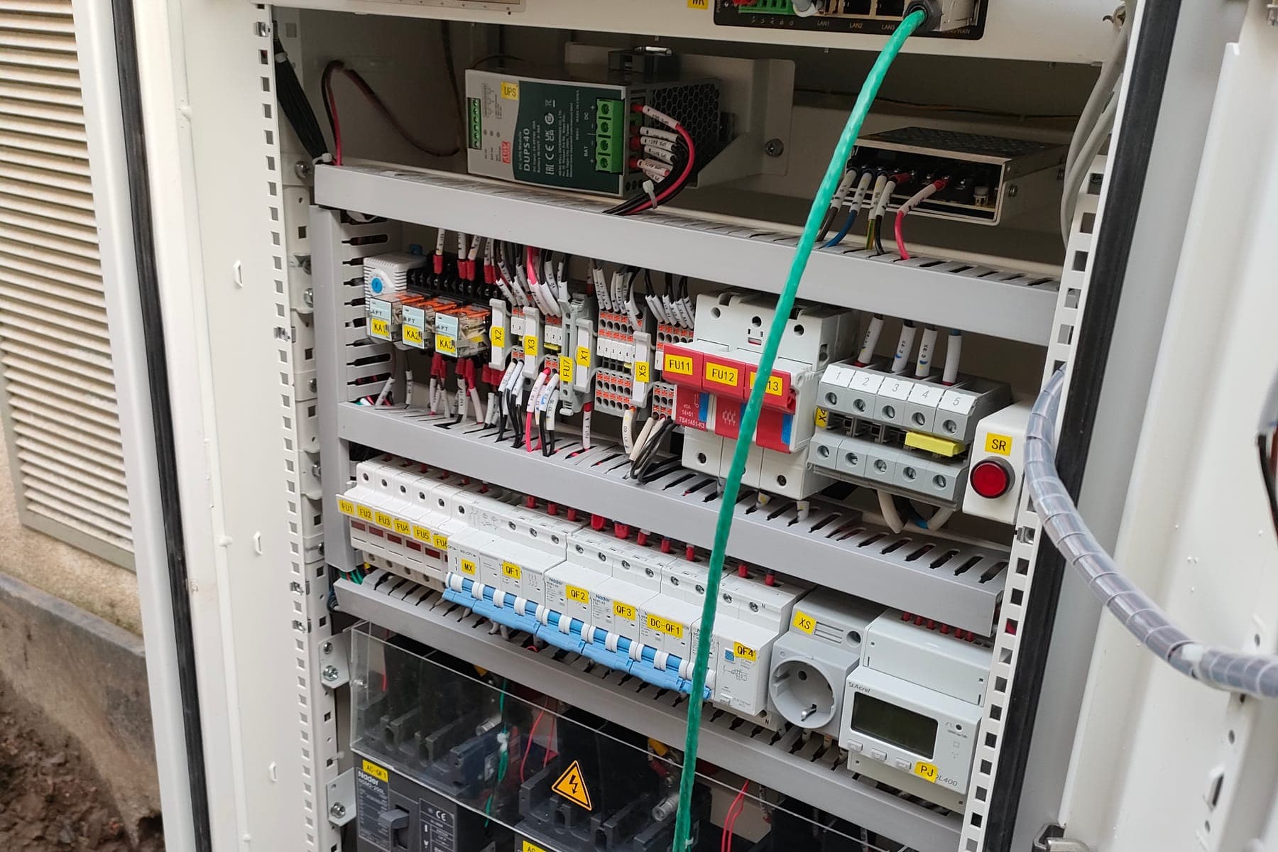 De schakel- en sturingskast van een batterijinstallatie, met gemerkte automaten en een monteur die een spanning meet