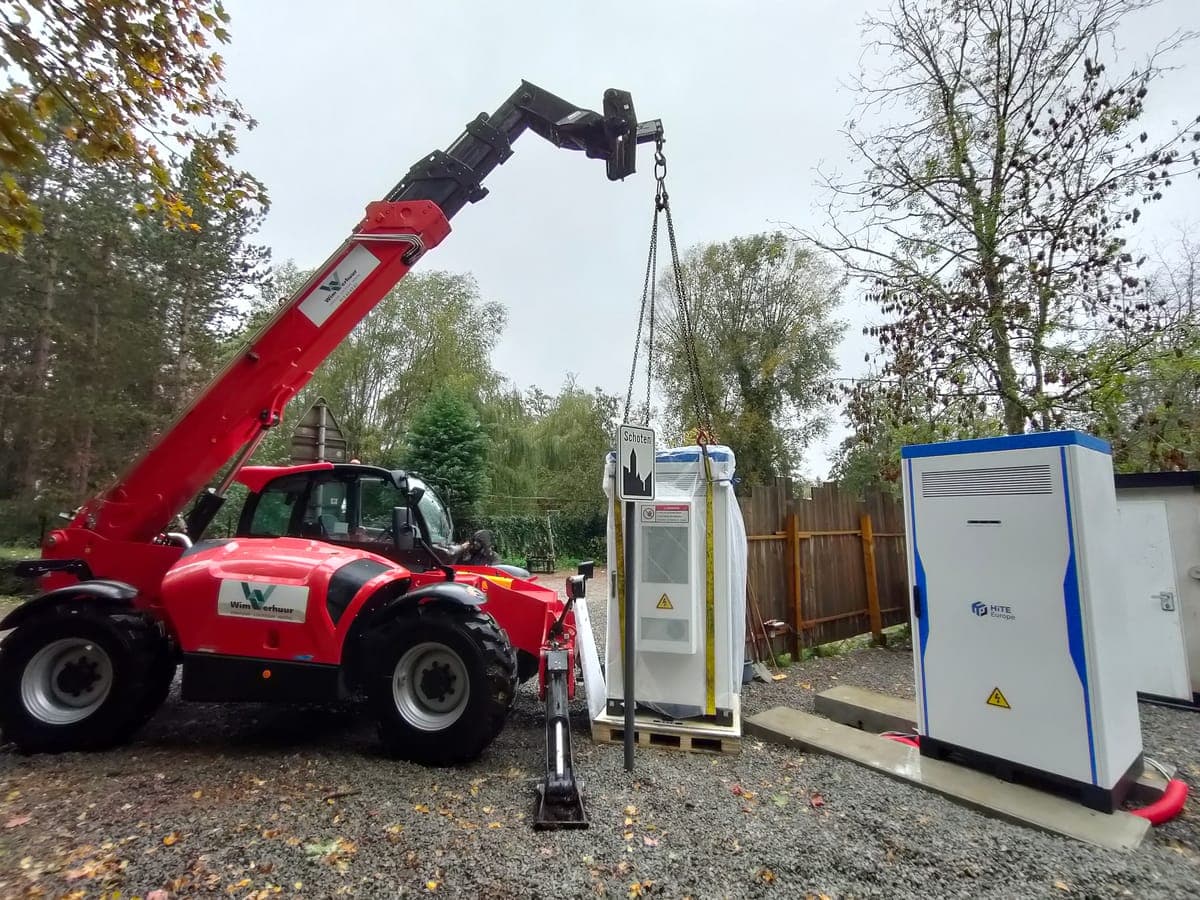 Een verreiker hijst een ingepakte batterijkast naast een kast die al geplaatst is