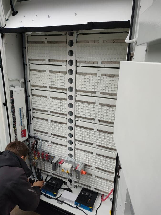 Een geopende batterijkast met de modules boven elkaar en een monteur aan de gelijkstroomaansluiting