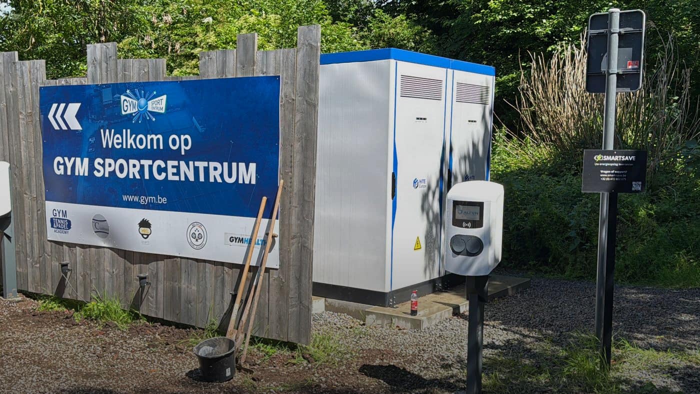 Twee batterijkasten met een laadpaal ernaast, naast het welkomstbord van het sportcentrum